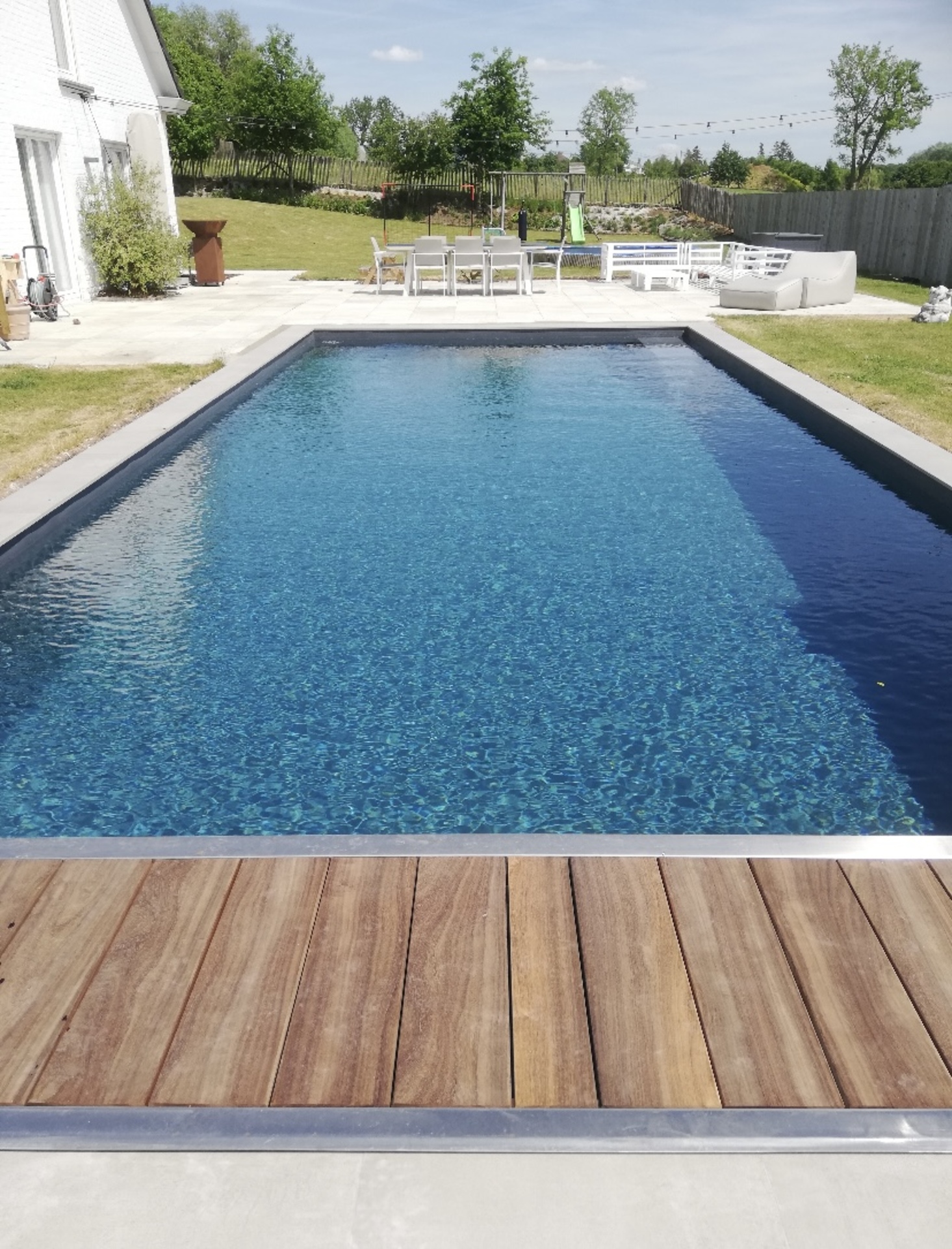 Lang rechthoekig zwembad met helderblauw water, natuurstenen boord en beplanting